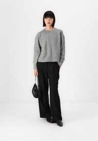 Grå strikkegenser med落ne skuldrer, parret med høyt liv svarte bukser. Svart håndveske med kjedehank, glatt tekstur, minimalistisk design.