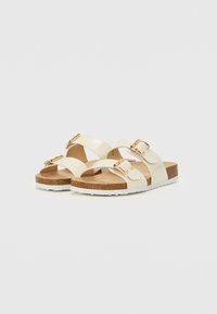 Lys beige sandaler med to justerbare remme og guldbuckles, med en korksål og en hvid gummisål.