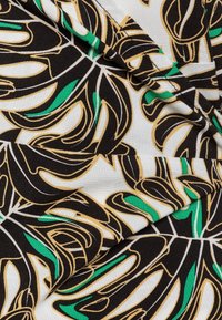 Tessuto con un audace motivo di foglie tropicali in nero, bianco, oro e verde, con una superficie liscia e pieghe sovrapposte.