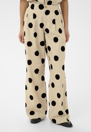 Pantaloni largi bej cu buline negre, purtați cu pantofi negri ascuțiți, văzuți de la talie până la picioare.