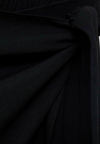 Svart tyg med en texturerad yta, som har veck och draperingar. Materialet verkar mjukt och lätt elastiskt, vilket framhäver djupet i färgen.