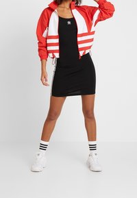 Röd och vit vindjacka med kraftiga ränder, i kombination med en åtsittande svart klänning och vita sneakers med svarta ränder.