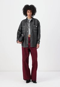 Czarna denimowa koszula z kontrastowym szwem, szary crop top z grafiką, czerwone szerokie spodnie i czarna torba. Modelka pozująca na neutralnym tle.