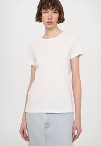 Tricou alb din bumbac cu decolteu rotund și mâneci scurte. Prezintă broderie subtilă pe piept și o croială lejeră.