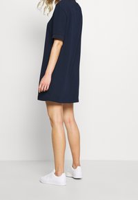 Marindress med kort ärm, krage, lös passform och knälång nederkant, kombinerad med vita sneakers. Slät tyg med en enkel design.