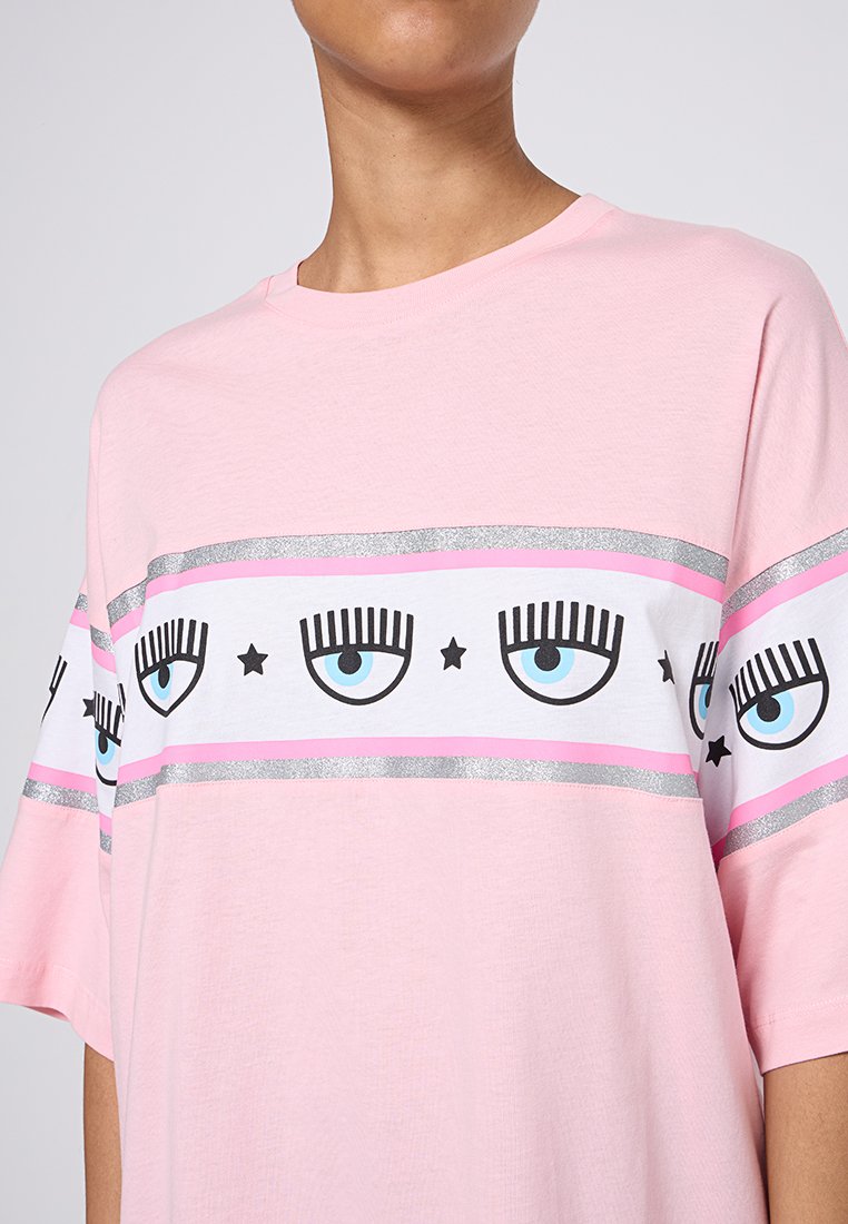 T-shirt en coton rose avec un design à rayures horizontales blanches et argentées, ainsi que des graphiques d'œil et d'étoile. Manches courtes, coupe décontractée.