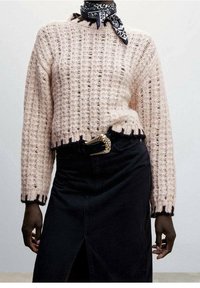 Maglione lavorato a maglia rosa chiaro con un motivo testurizzato, design corto e bordi neri sfilacciati, abbinato a una gonna nera con uno spacco frontale.