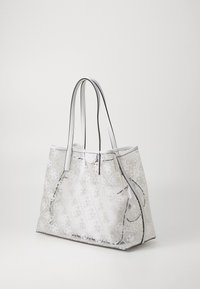 Sac cabas translucide avec motif géométrique blanc, accents argentés, et deux longues anses. Fabriqué en PVC durable avec une forme structurée.