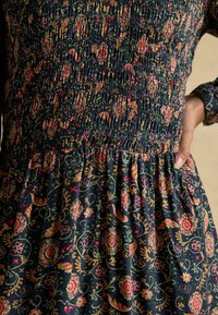 Marineblaues, gemustertes Kleid mit Smockdetails, das zarte Rosen und geschwungene Muster zeigt. Weicher, strukturierter Stoff mit einem ausladenden Rock.
