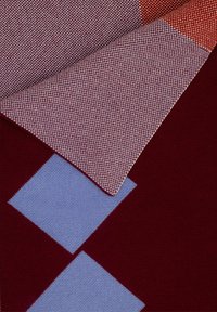 Tkanina z czerwonymi, niebieskimi i bordowymi geometrycznymi wzorami. Posiada teksturowaną powierzchnię oraz warstwowy design z wyraźnie kontrastującymi kolorami.