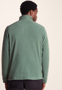 Green fleece pullover with a high collar, textured fabric, long sleeves, and a relaxed fit, viewed from the back.