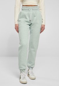 Ljust gröna sweatpants i mjukt material med hög elastisk midja, sidofickor och vita snoddar, i kombination med vita sneakers.