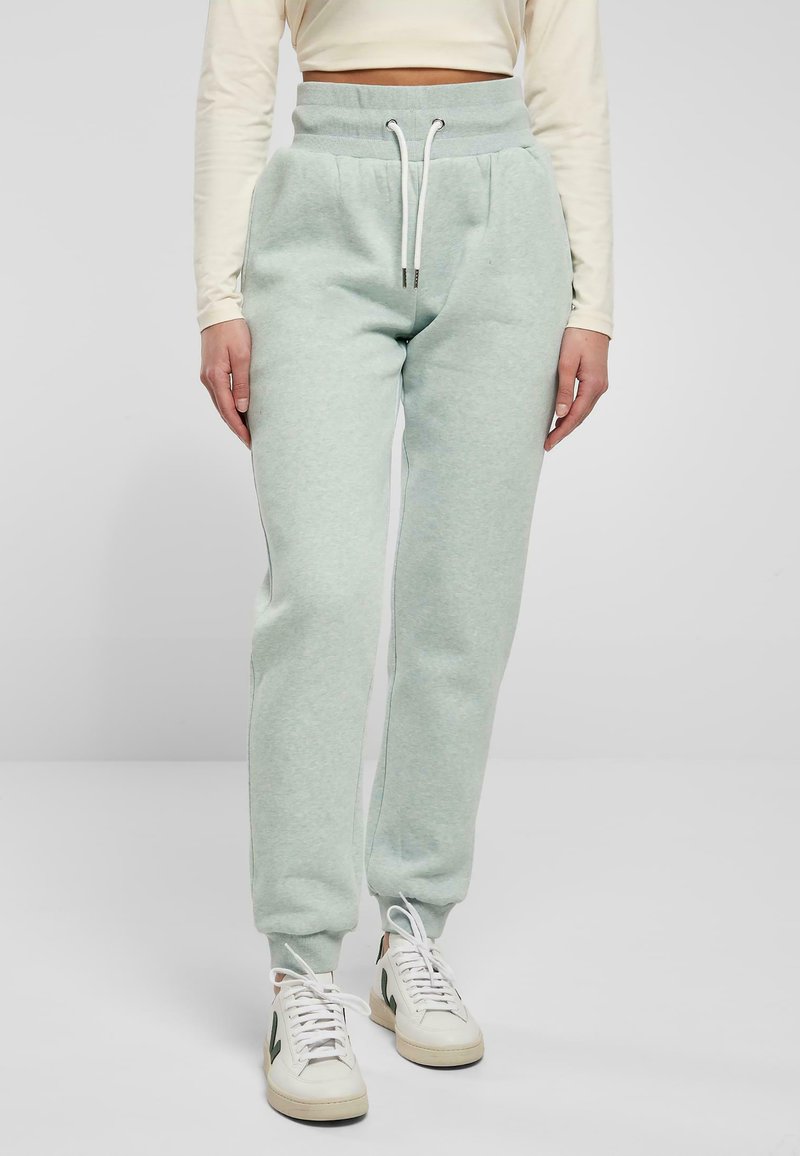 Ljust gröna sweatpants i mjukt material med hög elastisk midja, sidofickor och vita snoddar, i kombination med vita sneakers.