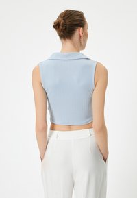 Top sin mangas de color azul claro, con relieve y corto, con cuello, combinado con pantalones ajustados blancos de cintura alta que cuentan con bolsillos laterales.