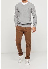 Pull gris à col en V porté sur un t-shirt blanc, associé à un chino marron et des baskets blanches. Le pull présente un petit logo sur la poitrine.