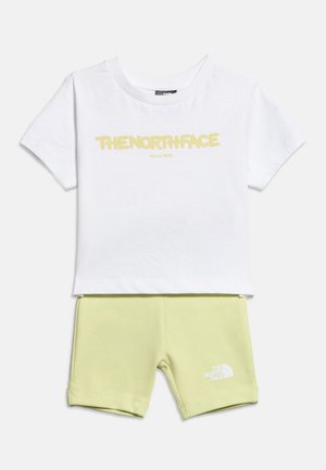 Balti trumpomis rankovėmis marškinėliai su geltonu užrašu „THENORTHFACE“ ir šviesiai žali šortai su baltu užrašu „The North Face“ ant kairės kojos.