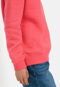 Korallenpinkes Sweatshirt mit gerippten Bündchen und Saum; bietet ein rundes "Home Sweet"-Grafikdesign in der Nähe des Handgelenks; aus weichem Baumwollmischmaterial.