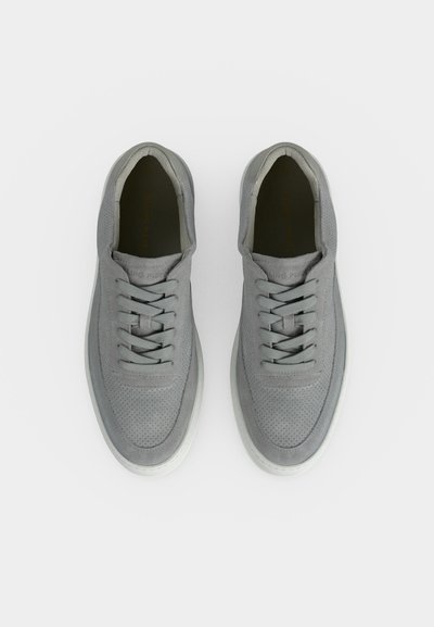 Ζευγάρι γκρι δερμάτινα αθλητικά παπούτσια με λευκές σόλες, δέσιμο μπροστά και διάτρητες λεπτομέρειες επάνω, από πάνω σε λευκό φόντο.