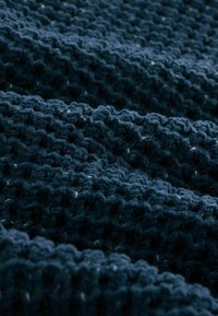 Tessuto lavorato a maglia blu scuro con un motivo a trama aperta e texturizzata, che presenta un aspetto morbido e peloso e sottili variazioni di colore.