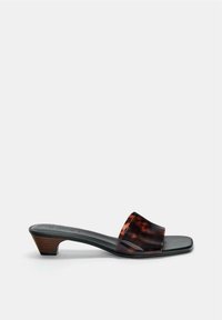 Sandale mule en cuir noir avec large bride en écaille de tortue et petit talon en bois empilé, vue de profil sur fond blanc.
