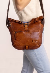 Brown leather crossbody bag with a textured surface, adjustable strap, and front zipper pocket. Features a buckle closure and logo accent.