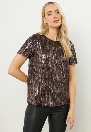 Bronzefarbenes Pailletten-Top mit kurzen Ärmeln, rundem Ausschnitt und strukturiertem Muster. Kombiniert mit schwarzen, figurbetonten Hosen.