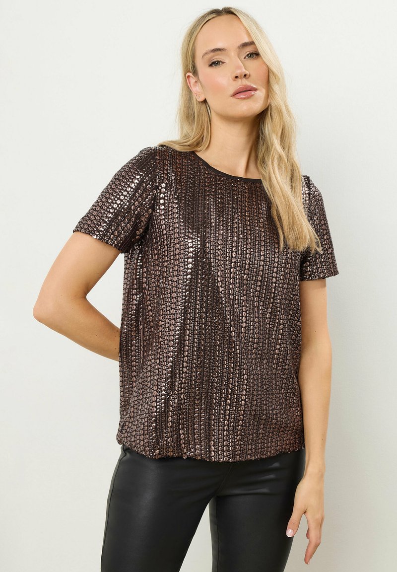 Bronze paljettop med korte ærmer, rund halsudskæring og et struktureret mønster. Sammen med sorte tætsiddende bukser.