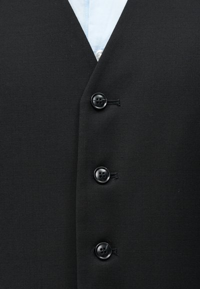 Μαύρο σακάκι κοστουμιού με τρία μαύρα κουμπιά, που αφήνει να φανεί ο γιακάς ενός ανοιχτό μπλε πουκάμισου από κάτω.