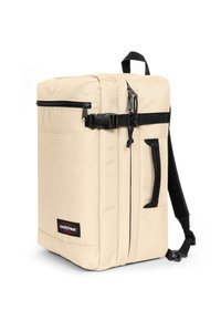 Mochila de tela beige con forma rectangular, detalles en negro, correas ajustables, bolsillo frontal con cremallera y etiqueta con el logo de Eastpak.