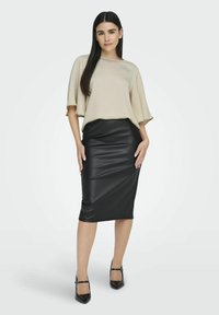 Beige top s krátkými, vykrojenými rukávy, kombinovaný s přiléhavou midi sukní z černé imitace kůže. Model má na sobě černé lodičky na kotníkovém pásku.