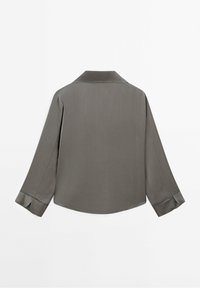 Chemise grise à manches longues avec col, poignets boutonnés et un ourlet légèrement arrondi, vue de dos sur un fond blanc.
