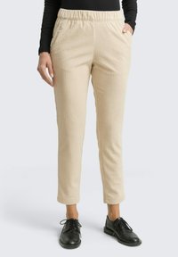 Beige corduroy broek met een elastische tailleband, slim-fit ontwerp, zijzakken en een gestructureerd oppervlak, gecombineerd met zwarte veterschoenen.