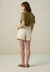 Chemise à manches courtes vert olive, shorts couleur crème et sandales à imprimé animal. Tissu doux et texturé, coupe décontractée avec des détails visibles dans le dos.