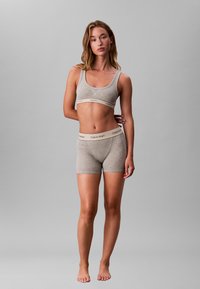 Sujetador deportivo gris de algodón y pantalones cortos a juego con una cinturilla elástica que presenta el logo de Calvin Klein. Textura suave, diseño sencillo.