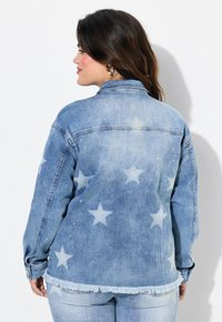 Chaqueta de denim azul claro con un patrón de estrellas, adornada con strass y con un dobladillo con flecos. Vista trasera mostrada.