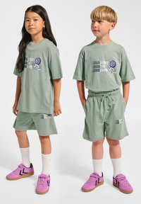 Ljusgröna bomulls-T-shirts med grafik som säger 'Serve the Game', matchade med byxor i samma färg. Skorna är rosa sneakers med vita strumpor.