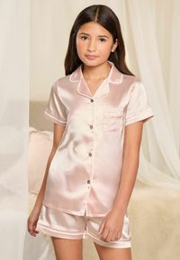 Svetloružový saténový krátky pyžamový set, ktorý obsahuje košelu na gombíky s vreckom a vyhrnutými rukávmi, spolu s nohavicami s hladkým povrchom.