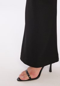 Zwarte, op maat gemaakte broekzoom met een gladde textuur, gecombineerd met een zwarte, gespen-sandaal met hoge hakken die een spitse neusdesign toont.