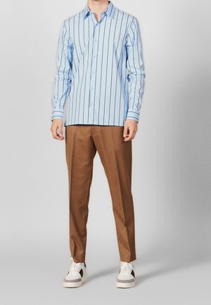 Chemise bleu clair à rayures navy, assortie à un pantalon marron ajusté et des baskets blanches avec des accents noirs.