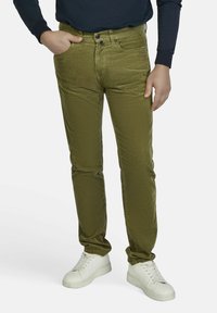 Olivgrüne Cordhose mit schmalem Bein, die über einen Knopfverschluss, Gürtelschlaufen und Seitentaschen verfügt, kombiniert mit weißen Sneakern.