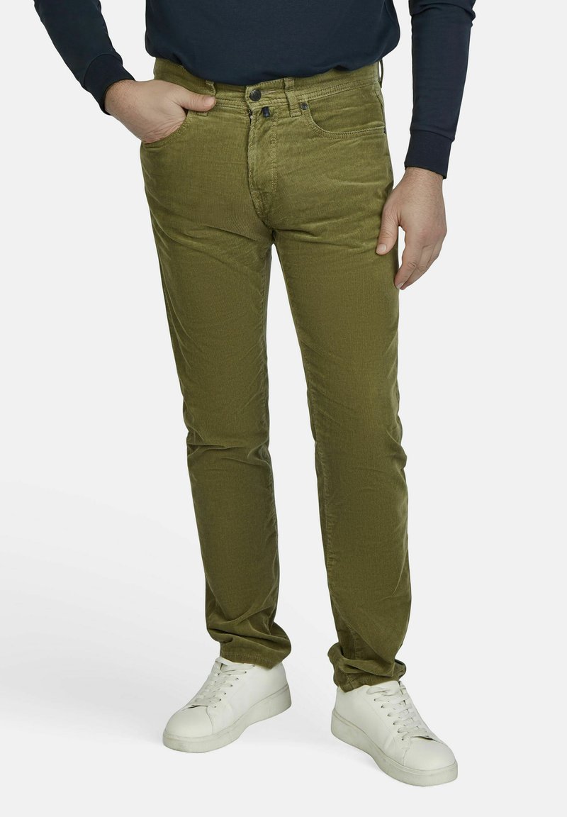 Olivgrüne Cordhose mit schmalem Bein, die über einen Knopfverschluss, Gürtelschlaufen und Seitentaschen verfügt, kombiniert mit weißen Sneakern.