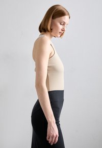 Beige mouwloos topje gecombineerd met een hoge taille zwarte rok. Soepele stof, aansluitend ontwerp en eenvoudige lijnen zijn benadrukt.