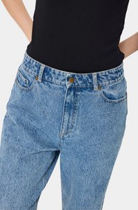 Svijetloplave traperice visokog struka s izblijedjelom teksturom, s prednjim kopčanjem na dugme, pet džepova i suptilnim detaljima šavova.