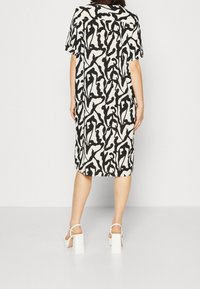 Kleid mit kurzen Ärmeln in Weiß mit abstraktem schwarzem Muster. Es hat eine lockere Passform und reicht knapp über die Knie, kombiniert mit weißen Sandalen mit klobigem Absatz.