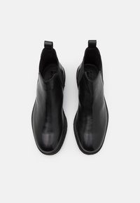 Bottes Chelsea en cuir noir à finition lisse, bout arrondi, panneaux latéraux élastiques et languettes pour un enfilage facile. Semelle en caoutchouc plate.