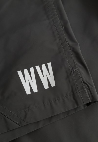 Μαύρο ύφασμα με λευκό λογότυπο "WW" τυπωμένο κοντά στη ραμμένη ένωση και την διπλωμένη άκρη.