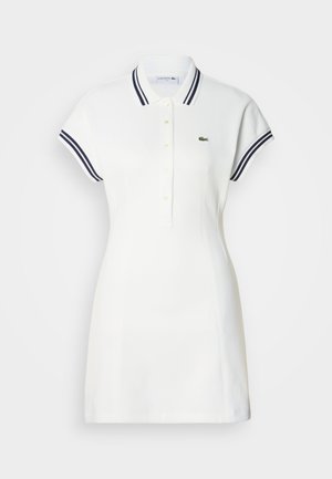 Vestido tipo polo blanco con mangas cortas, cuello a rayas azul marino, tapeta con cuatro botones y logo de cocodrilo bordado en verde en el pecho izquierdo.