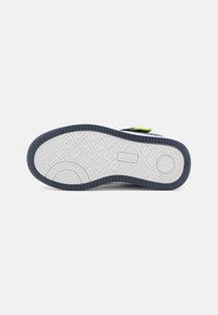 Witte sneakerzool met een patroon voor grip, voorzien van een marineblauwe rand en een groene accenten bij de hiel. Glad oppervlak, rubber materiaal.