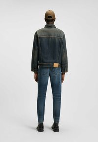 Jeansjacka med medelblå tvätt, kontrasterande sömmar och lädermärke. I kombination med mörkblå slim-fit jeans och svarta stövlar.