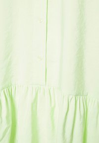 Vestido verde claro com botões e textura franzida na parte inferior. Feito de um tecido suave, possui um corte descontraído e superfície lisa.